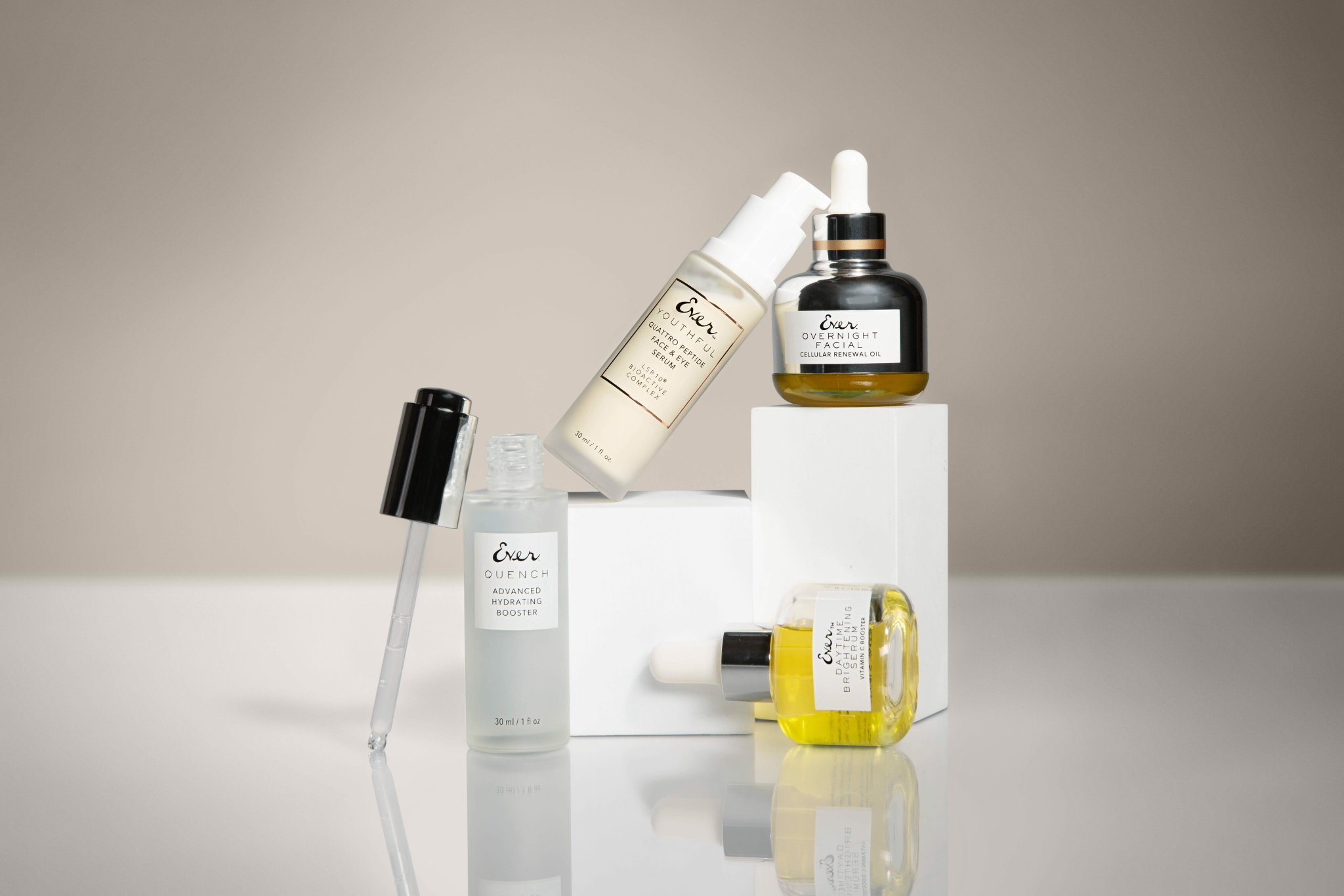 An image of QUENCH Advanced Hydrating Booster, Youthful Quattro Peptide, OVERNIGHT FACIAL Cellular Renewal Oil, and DAYTIME Brightening Serum on a Gray and white Background .